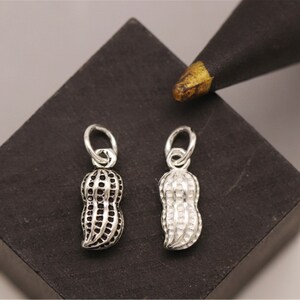 May include: Two silver peanut charms with a textured surface. The charms are on a black surface.