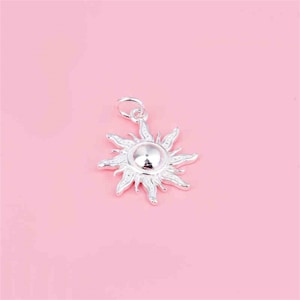 May include: Silver sun charm pendant with a detailed design. The charm is a stylized sun with rays extending from the center.