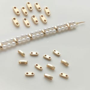 Op de afbeelding: Goudkleurige metalen connector kralen voor het maken van sieraden. De kralen hebben twee gaten aan elke kant en zijn ovaalvormig.