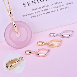 May include: A set of three gold-tone pendant charms with a teardrop shape and a curved bar. The charms are on a pink surface. The charms are marked with "925".