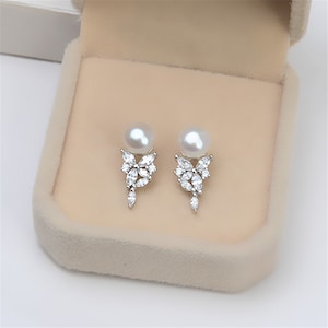 Puede incluir: Un par de pendientes de plata con una perla y un racimo de piedras de circonita cúbica transparentes.