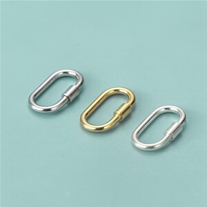 May include: Three oval-shaped carabiner clasps in silver and gold tones. The clasps have a screw-lock mechanism for secure closure. The background is a solid light teal color.