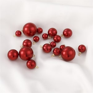 May include: A collection of red pearl beads with gold accents. The beads are of various sizes and are scattered on a white surface.