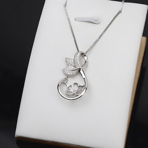 Op de afbeelding: Een zilveren ketting met een hanger met een delicaat bloemmotief met een parelbezetting en een bladmotief met heldere zirkonia-stenen.