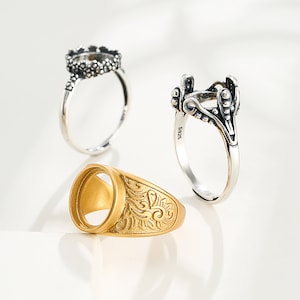 Puede incluir: Tres anillos de plata con diseños ornamentados y engastes abiertos para piedras. Los anillos están sobre una superficie blanca.