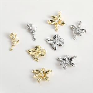 Puede incluir: Una variedad de dijes con forma de flor en tonos dorados y plateados, algunos con pequeñas piedras preciosas transparentes. Los dijes incluyen diseños de rosas y flores, perfectos para la creación de joyas o proyectos de manualidades.