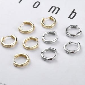 May include: Eight hoop earrings, four gold and four silver, with a geometric design. The earrings are arranged in two rows on a white surface.