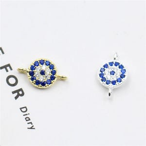 Könnte beinhalten: Zwei böse Augen-Anhänger mit blauen und weißen Steinen. Ein Anhänger ist golden, der andere silbern.