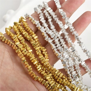 May include: Close-up of gold and silver rhinestone trim. The trim is made of small, rectangular rhinestones arranged in a linear pattern. The gold trim has a textured appearance, while the silver trim sparkles. The trim is held in a hand.