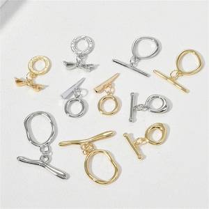 Pode incluir: Conjunto de fechos de correr de metal dourado e prateado com diferentes formas e designs. Alguns fechos têm um anel, enquanto outros têm uma barra ou um laço. Estes fechos são perfeitos para a criação de joias ou outros projetos de artesanato.