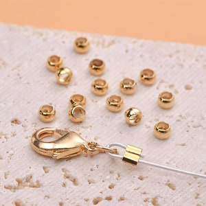 Pode incluir: Contas de metal dourado e um fecho para fazer joias. As contas são redondas e têm um acabamento liso. O fecho é do tipo lagosta.