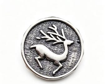 May include: A silver-colored round pendant featuring a detailed image of a deer with large antlers. The deer is depicted in a leaping pose within a textured circular frame. The pendant has a vintage or antique appearance.