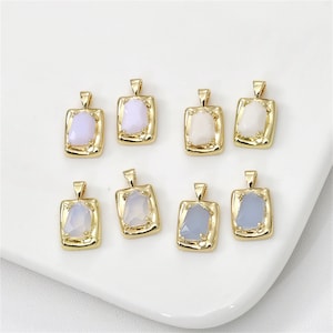 May include: Eight gold pendants with different colored glass stones. The pendants are square shaped with a textured gold frame.