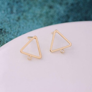 May include: Two gold-colored, open-frame triangle earrings. Each earring has a post for insertion and a small loop at the bottom corner for attaching additional elements. The earrings are set against a white surface.