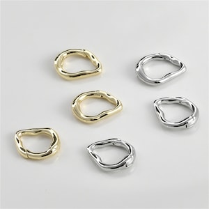May include: Six gold and silver metal rings with an irregular, wavy shape. The rings are open and have a spring closure.