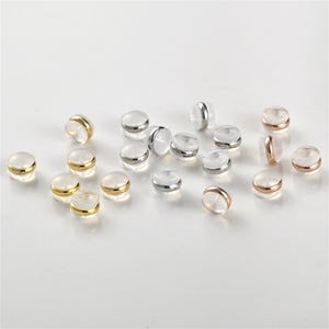 May include: Assortment of clear plastic earring backs with gold, silver, and rose gold trim.