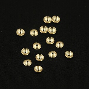 May include: A group of 15 gold-colored metal bead caps scattered on a black surface. The caps are round with a flat top and a small hole in the center.