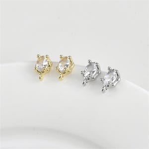 May include: Two pairs of earrings with a clear oval-shaped stone set in a gold or silver crown-like setting. The earrings have a loop for attaching to a chain or other jewelry.