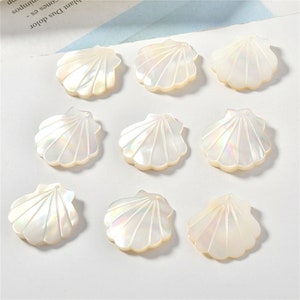 Pode incluir: Dez pingentes de concha branca com um furo para enfiar. As conchas têm um acabamento perolado e são em forma de vieiras.