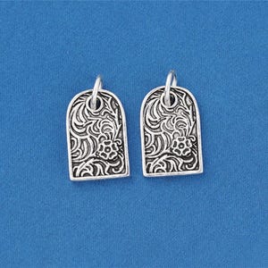 May include: Two silver-toned metal charms, each featuring an arched rectangular shape with a raised, intricate floral and scrollwork pattern. Each charm includes a small circular jump ring attached at the top for hanging or connecting to jewelry.