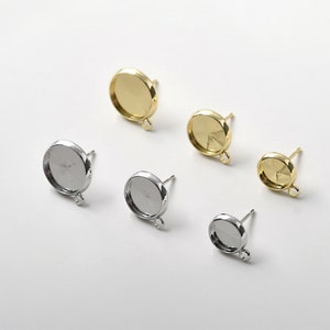 May include: Five round, silver and gold earring settings with posts and loops. The settings are different sizes.