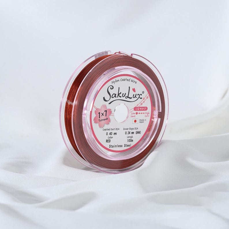 May include: A spool of red nylon-coated wire, labeled "SakuLux," is displayed against a white background. The label indicates the wire is 0.40 mm in diameter and 100 m in length. The spool is made of stainless steel.