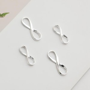 Pode incluir: Quatro pingentes de prata em forma de símbolo de infinito, cada um com uma torção ligeiramente diferente, perfeitos para fazer joias.
