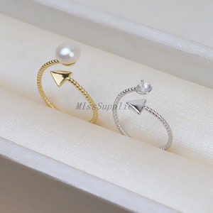 May include: Two silver rings with a twisted design. One ring has a pearl attached to the top, while the other ring has a blank setting for a pearl.