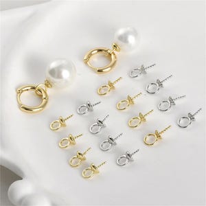 Könnte beinhalten: Ein Satz Ohrring-Verschlüsse aus Gold und Silber mit einer Perle an einem Creolen-Ohrring. Die Verschlüsse haben eine kleine Schlaufe und einen Schraubstift.