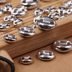 May include: A close-up of silver metal beads with two holes in each bead. The beads are arranged on a wooden surface.