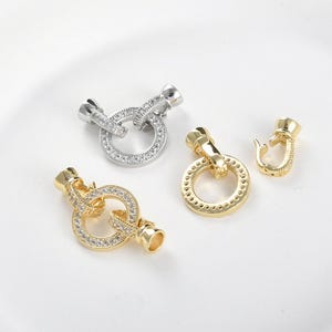 Può includere: Due chiusure in metallo color argento e oro con un design rotondo. La chiusura argentata è incrostata di strass trasparenti. La chiusura dorata è liscia.