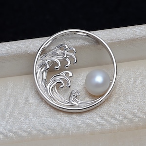 May include: A silver pendant featuring a wave design with a white pearl in the center. The pendant is circular and has a delicate, intricate design.