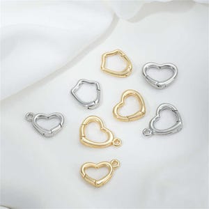 May include: Assortment of silver and gold heart-shaped metal clasps. The clasps are open and ready to be attached to a chain or other jewelry.