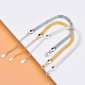 May include: Three silver chain bracelets with different colored clasps: silver, gold, and black. The bracelets are laid out on a white surface.
