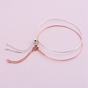 May include: Two adjustable bracelets with a silver and rose gold finish. The bracelets have a delicate chain with a small bead at the end.