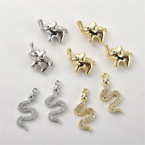Può includere: Un set di ciondoli a forma di elefante e serpente in argento e oro. I ciondoli a forma di elefante hanno una proboscide rialzata e sono dettagliati con occhi neri. I ciondoli a forma di serpente sono dettagliati con strass trasparenti.