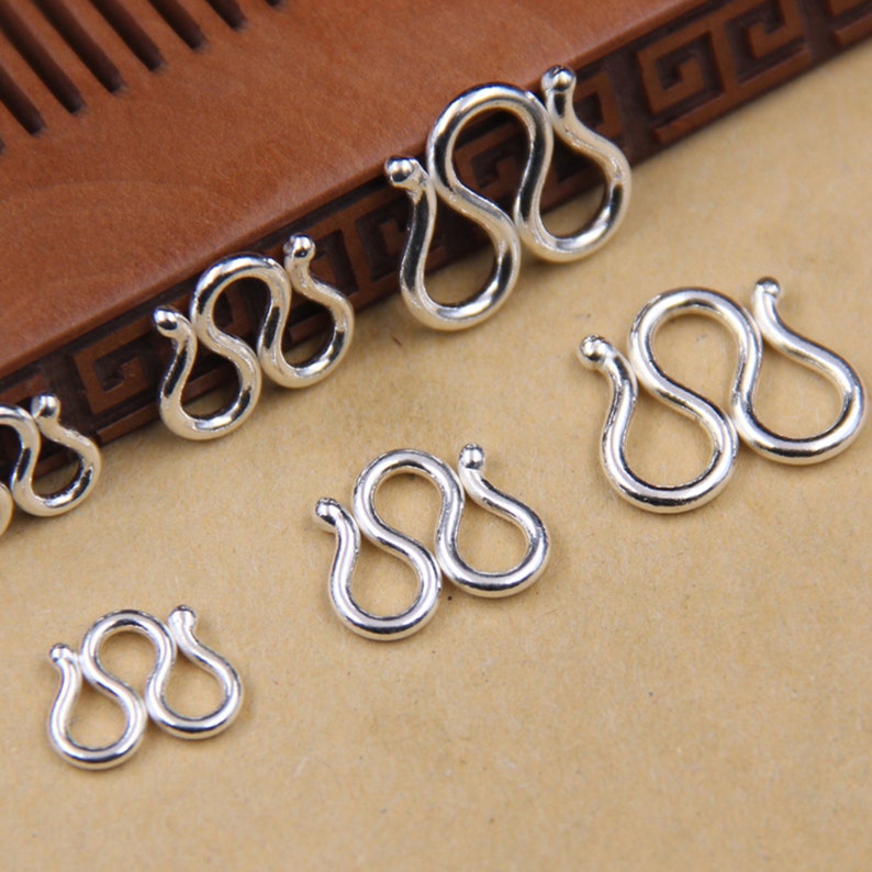 May include: A set of six silver-toned metal lobster clasps in various sizes. The clasps are shaped like a figure eight and are designed to be used for jewelry making.