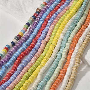 Peut inclure: Une collection de perles en céramique colorées dans différentes nuances de bleu, vert, jaune, rose, rouge et blanc. Les perles sont enfilées sur un fil blanc et sont disposées en rangées.