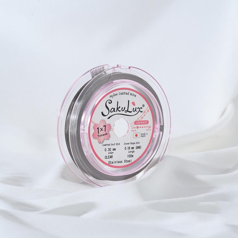 May include: A clear, nylon-coated wire spool with the brand name "SakuLux" printed on the label. The label also indicates the wire is 0.30 mm in diameter and 100m in length. The spool is encased in a clear, pink plastic container.