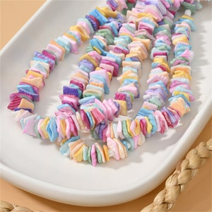May include: A strand of colorful, iridescent, square-shaped beads made from natural seashells. The beads are strung on a clear elastic cord and are perfect for making jewelry.