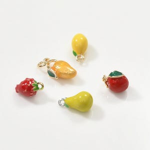 May include: A collection of colorful fruit charms, including a red strawberry, a yellow lemon, a yellow pear, a red apple, and an orange mango. Each charm has a small loop for attaching to jewelry or other crafts. The charms are brightly colored and have a glossy finish.