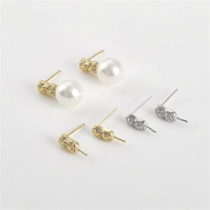 May include: A set of four earring findings with a pearl and a gold or silver post. The findings are decorated with small clear rhinestones.