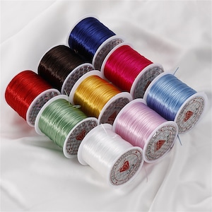 Könnte beinhalten: Sortiment an bunten elastischen Schnurspulen, jede mit einem weißen Etikett mit der Aufschrift "Strong & Stretchy".