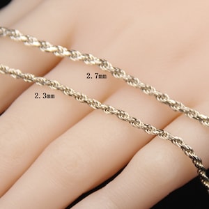 May include: Close-up of two gold-colored rope chains, one 2.3 mm and the other 2.7 mm thick. The chains are displayed against a neutral background. The image highlights the texture and design of the jewelry.
