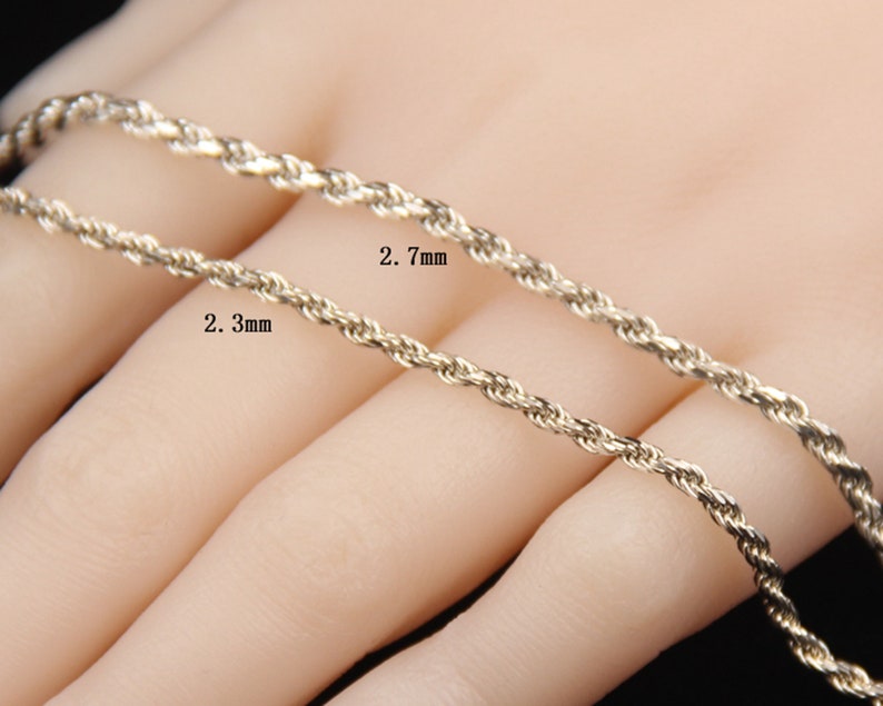 May include: Close-up of two gold-colored rope chains, one 2.3 mm and the other 2.7 mm thick. The chains are displayed against a neutral background. The image highlights the texture and design of the jewelry.