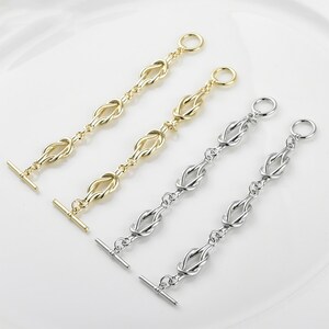 May include: Four metal toggle clasps. Two are gold-toned, and two are silver-toned. Each clasp features a series of knot-shaped links connected by small chain segments. The clasps have a T-bar closure on one end and a ring on the other.