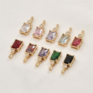 Könnte beinhalten: Sortiment von zehn goldfarbenen Anhänger-Anhängern mit einer Vielzahl von rechteckigen Edelsteinen in verschiedenen Farben. Jeder Anhänger hat oben einen kleinen klaren Strassstein.