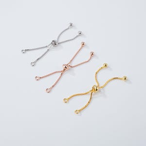 May include: Three adjustable bracelet clasps in silver, rose gold, and gold. Each clasp features a central bead, two strands of chain, and a small bead at the end of each strand. These clasps are for jewellery making.