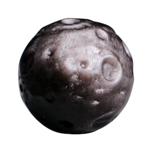 May include: A black and grey moon-shaped stress ball with a textured surface and craters.