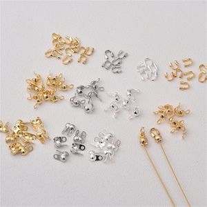 Könnte beinhalten: Sortiment an goldenen und silbernen Schmuck-Findings, darunter Crimp-Perlen, Sprungringe und Verschlüsse. Diese Findings sind perfekt für die Herstellung von Halsketten, Armbändern und Ohrringen.
